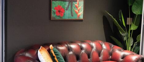 A dark-themed room with a leather sofa, a wooden dining table, and a large plant.