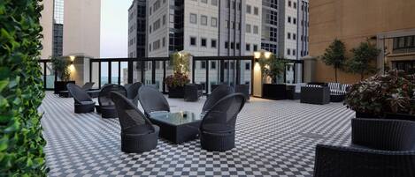 An outdoor seating area with checkered flooring, wicker furniture, and potted plants.