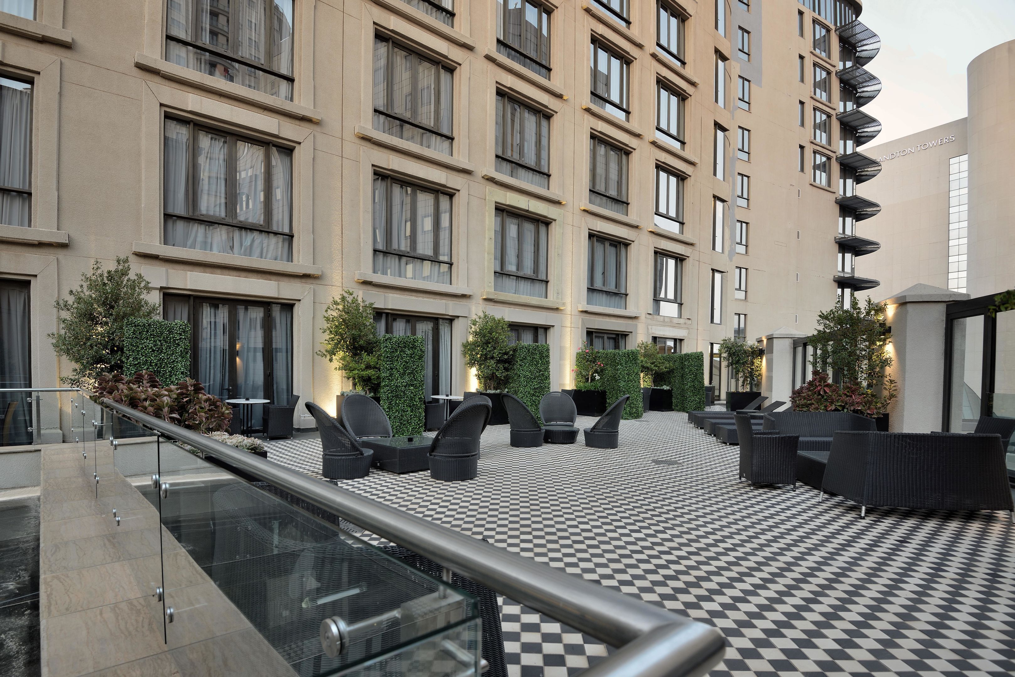 Un patio de hotel moderno con suelo a cuadros, mobiliario exterior y barandilla de vidrio.