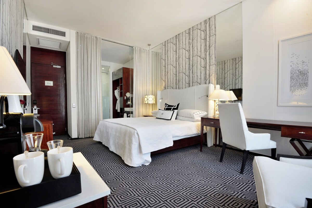 A hotel room with a large bed, a desk, a chair, and a coffee station.