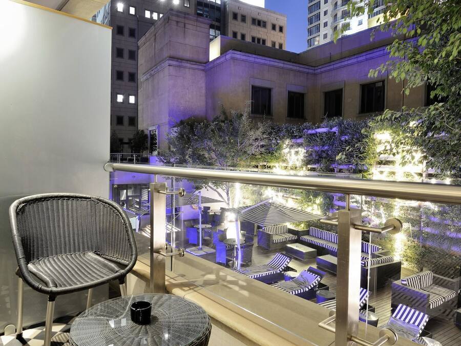 Un balcón con suelo a cuadros, mobiliario de mimbre y vistas a un edificio con ventanas iluminadas.
