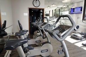 A gym with multiple exercise machines, a clock on the wall, and a digital display. - Davinci Hotel And Suites On Nelson Mandela Square (Sandton)