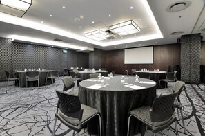 Un salón de conferencias con mesas redondas, sillas y una pantalla para proyector.