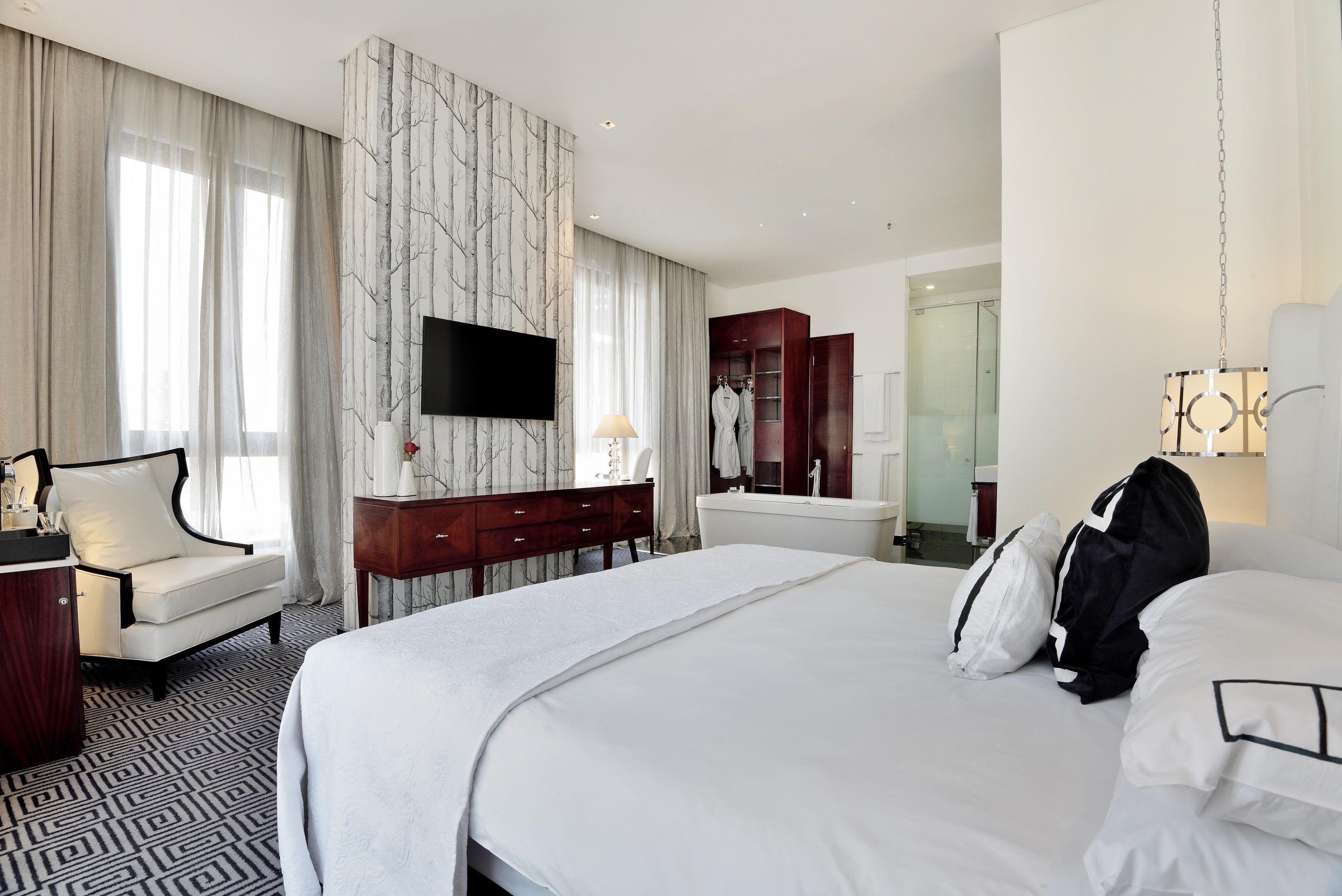 A hotel room with a large bed, a desk with a chair, a wardrobe, a mirror, and a TV on the wall.