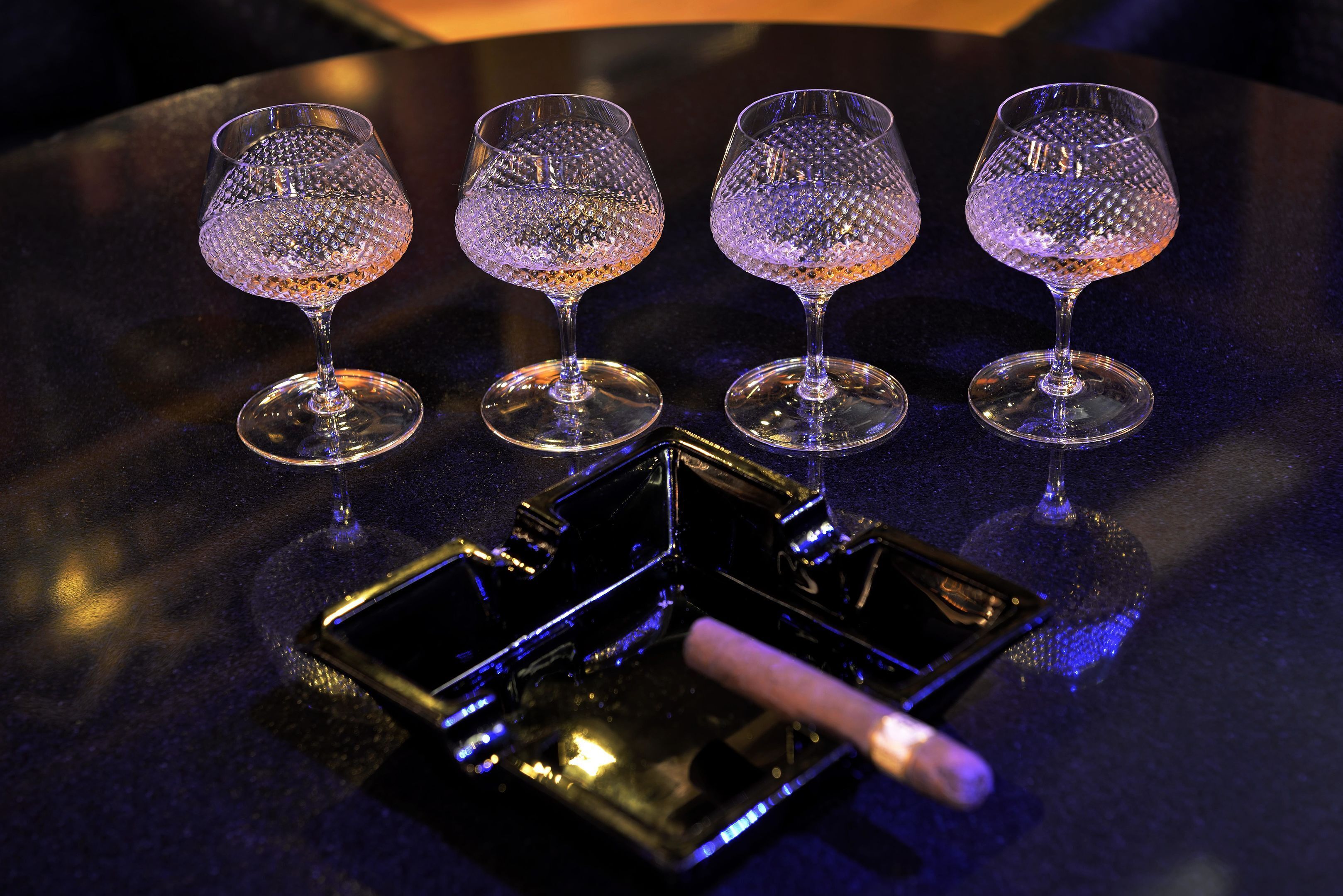 Three clear glass wine glasses on a dark surface with a tray and a smartphone.