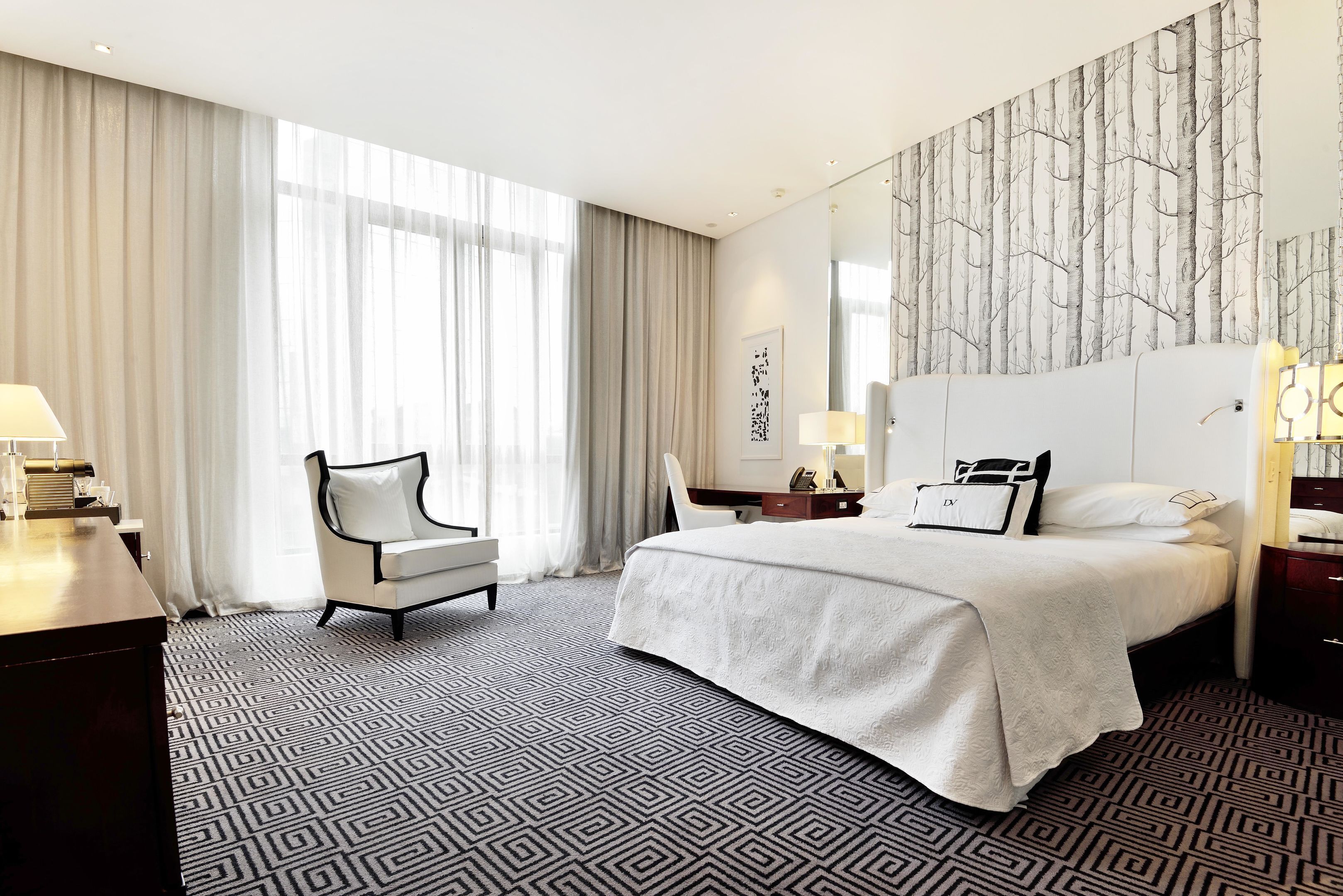A hotel room with a large bed, a desk, a chair, and a large window with curtains.