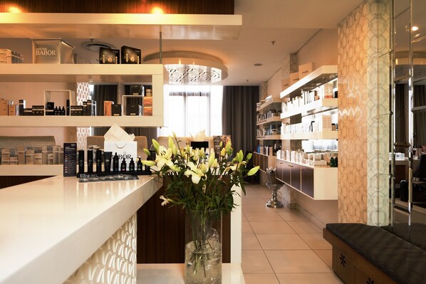 A modern hotel lobby with a reception desk, shelves with toiletries, and a vase of flowers.