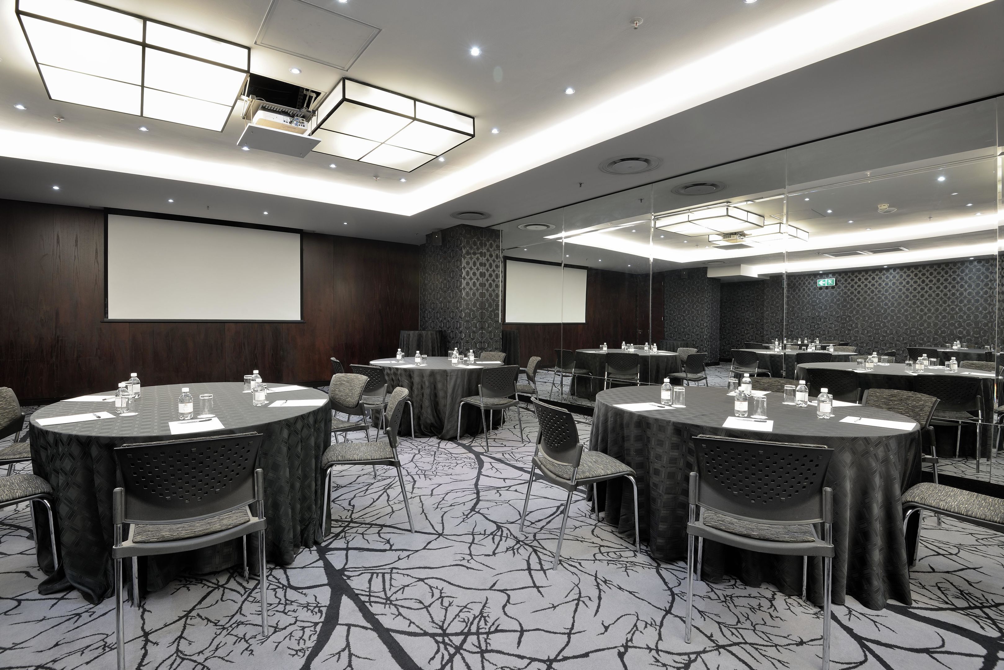 A conference room with multiple round tables, chairs, and a large screen.