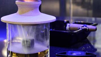 A glass container with a wooden lid on a reflective surface, accompanied by a black tray with a rolled-up item and a metal object.