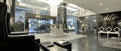 A modern lobby with a black leather sofa, a round white table, and a glass wall with the 'ilifa COLLECTIVE' sign.