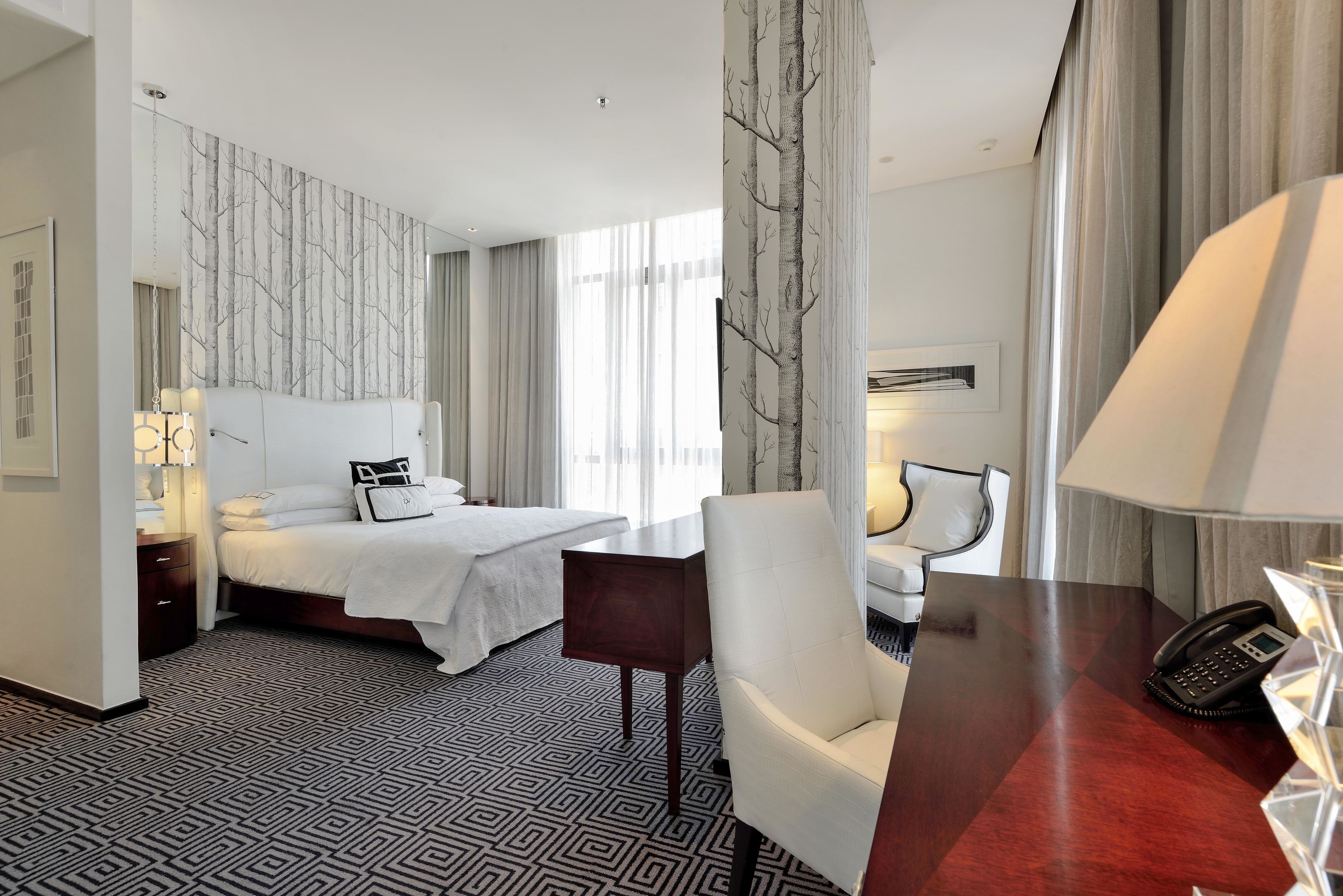 Une chambre d’hôtel avec un lit, un bureau, une chaise, un téléphone et une lampe.