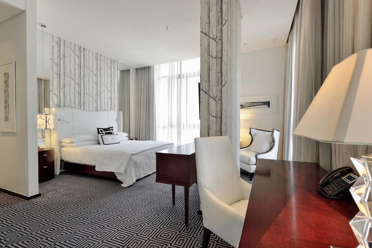 Une chambre d’hôtel avec un lit, un bureau, une chaise, un téléphone et une lampe.