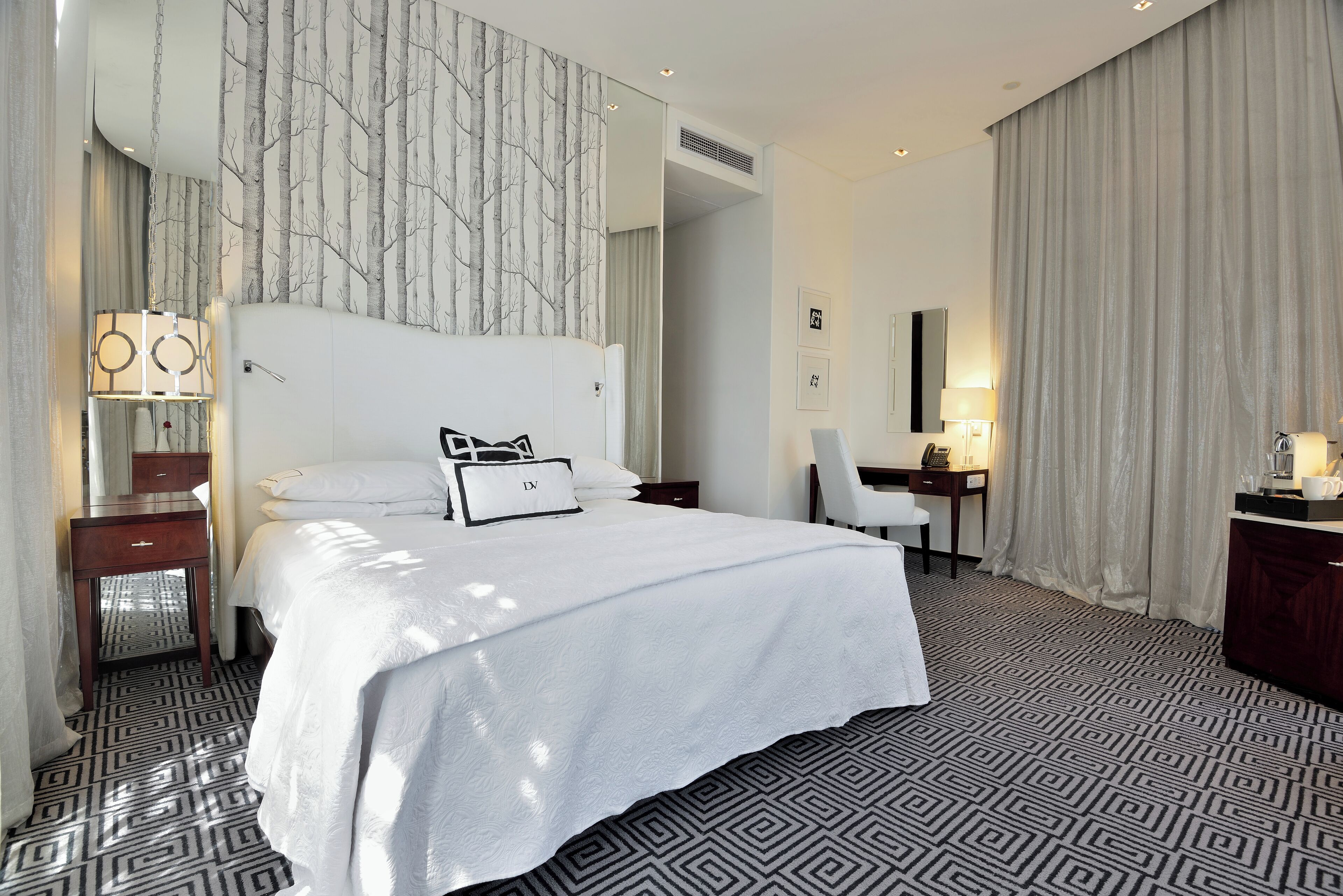 A hotel room with a large bed, a desk, a chair, and a wardrobe.