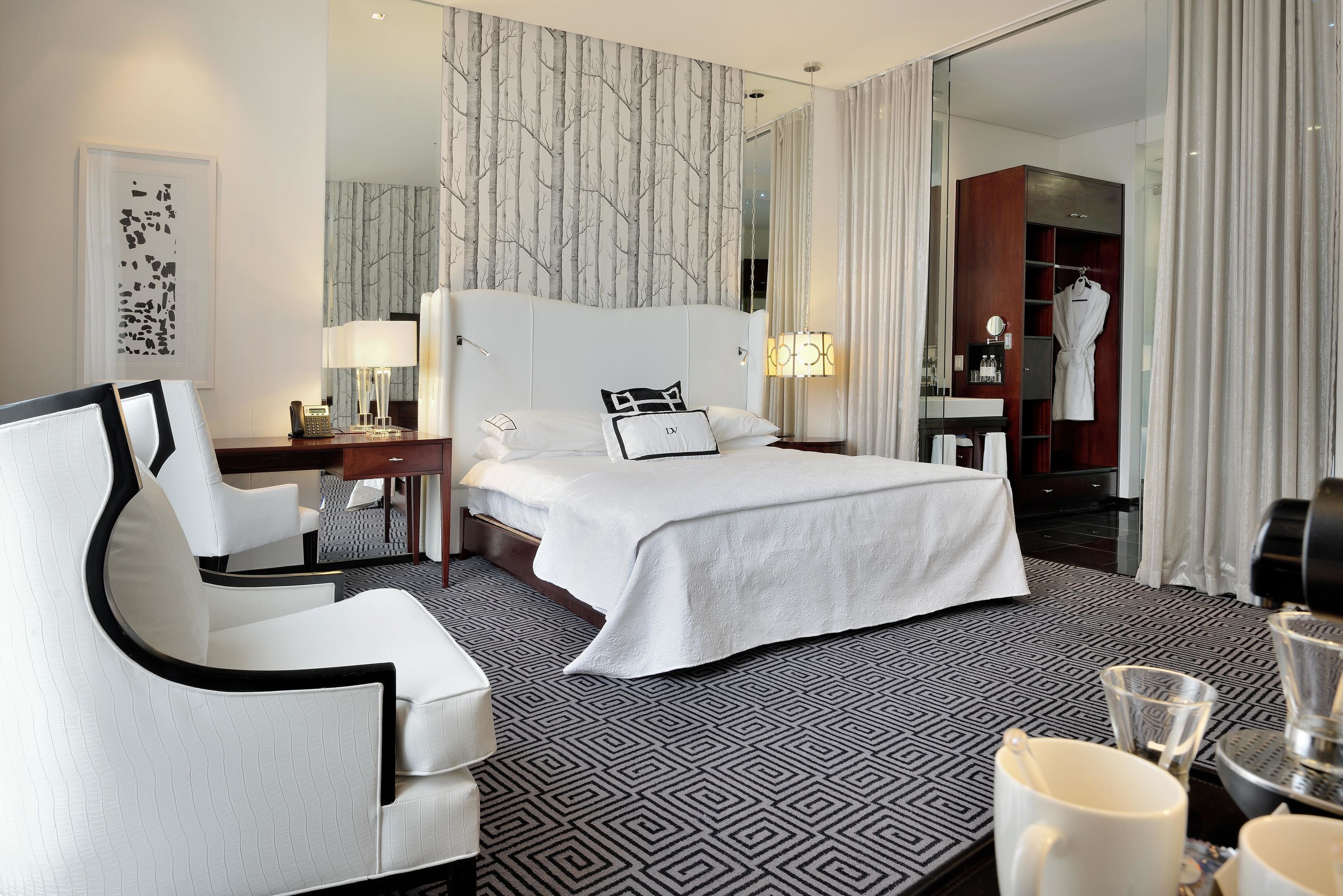 Une chambre d’hôtel avec un grand lit, un fauteuil blanc, un bureau avec une lampe et une armoire.