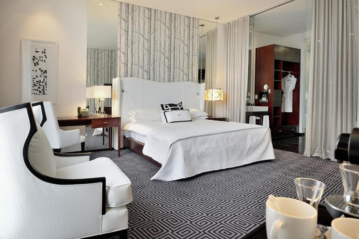 Une chambre d’hôtel avec un grand lit, un fauteuil blanc, un bureau avec une lampe et une armoire.