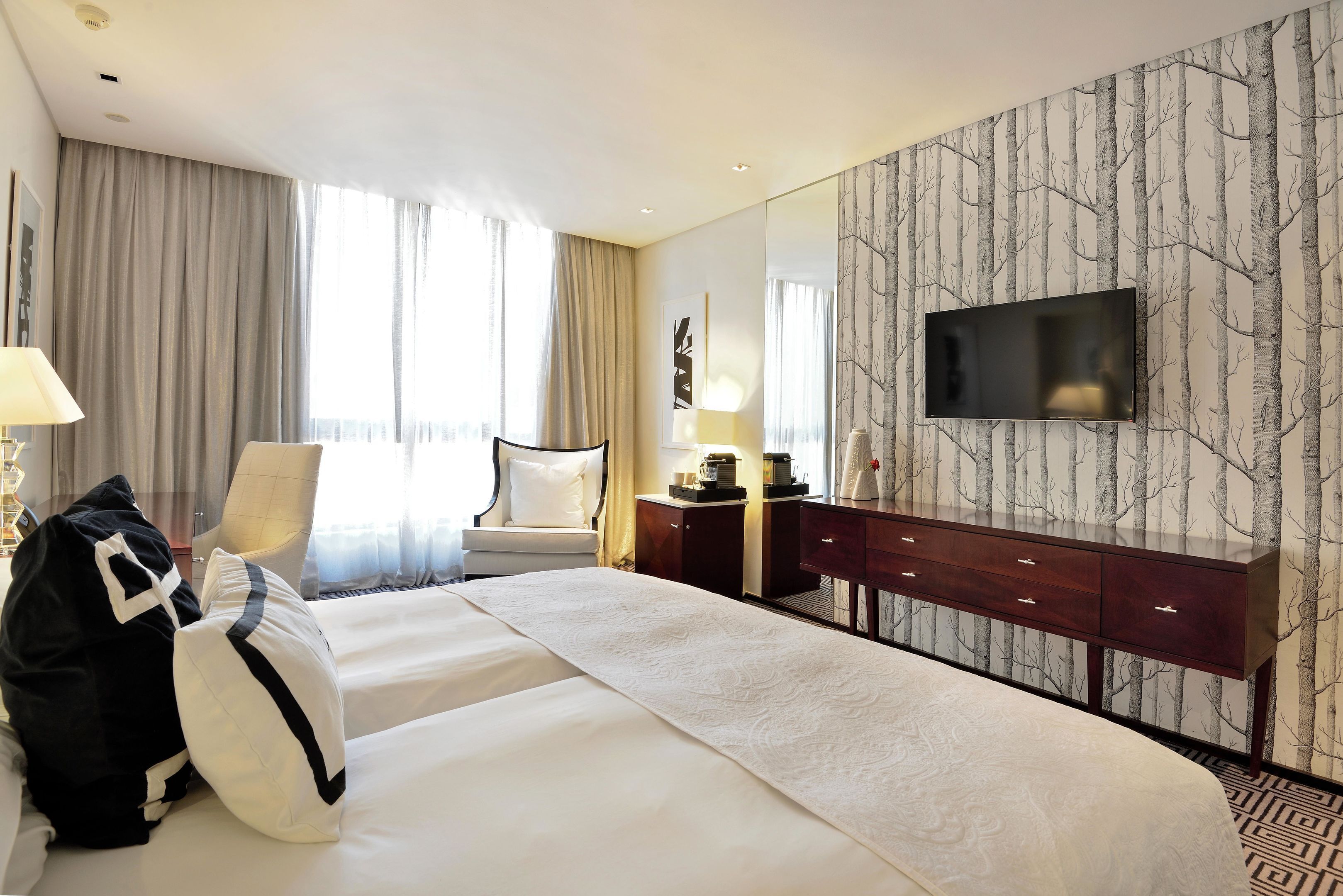 A hotel room with a large bed, a TV mounted on the wall, a desk with a lamp, and a chair.