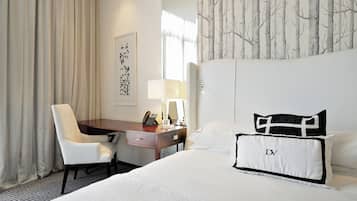 Habitación de hotel con cama, escritorio, silla, lámpara y un papel tapiz con diseño de árbol.