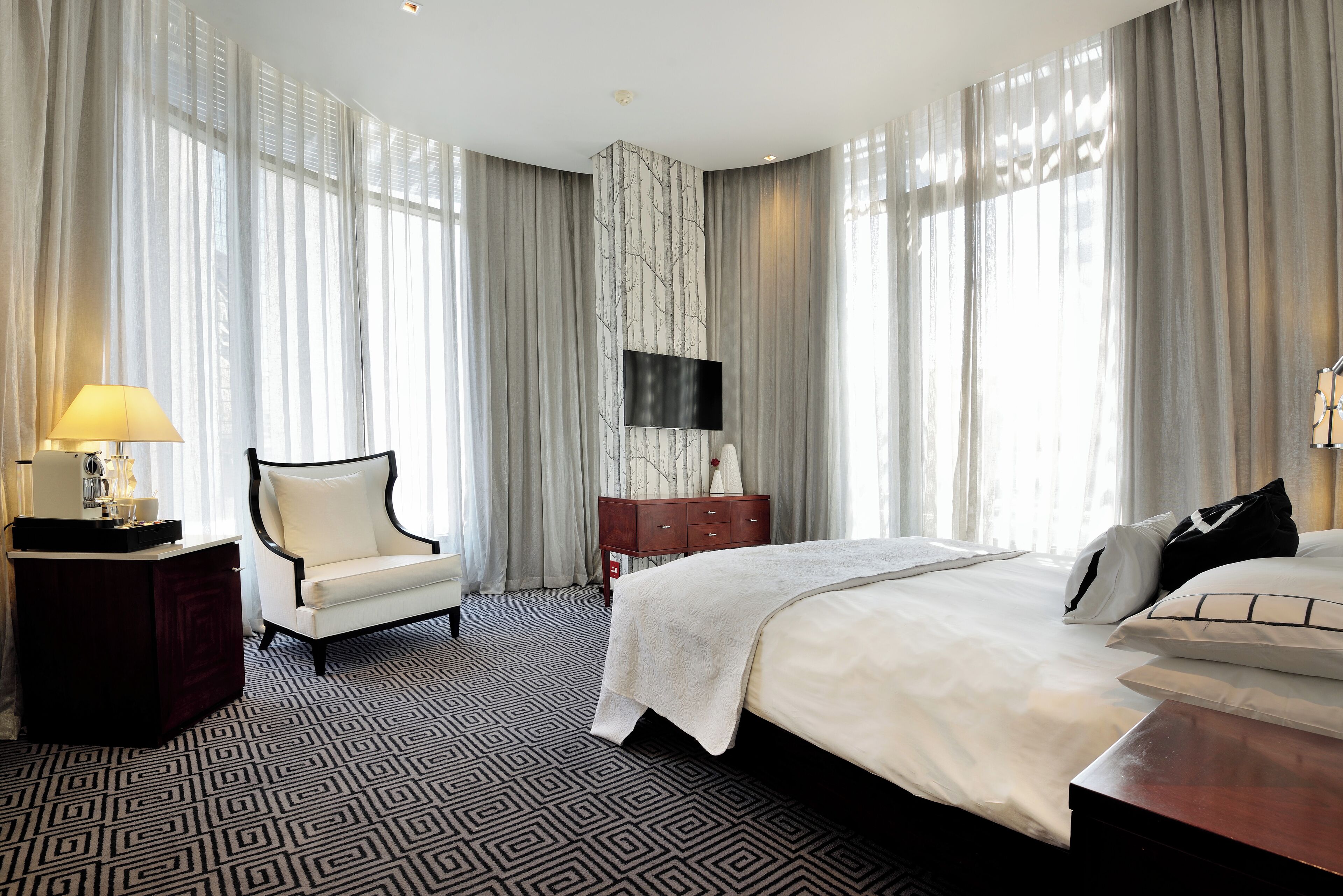 A hotel room with a large bed, a chair, a dresser, and a TV mounted on the wall.