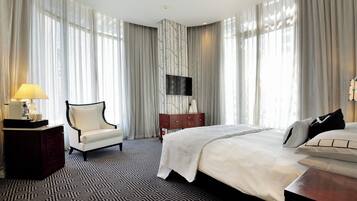 A hotel room with a large bed, a chair, a dresser, and a TV mounted on the wall.