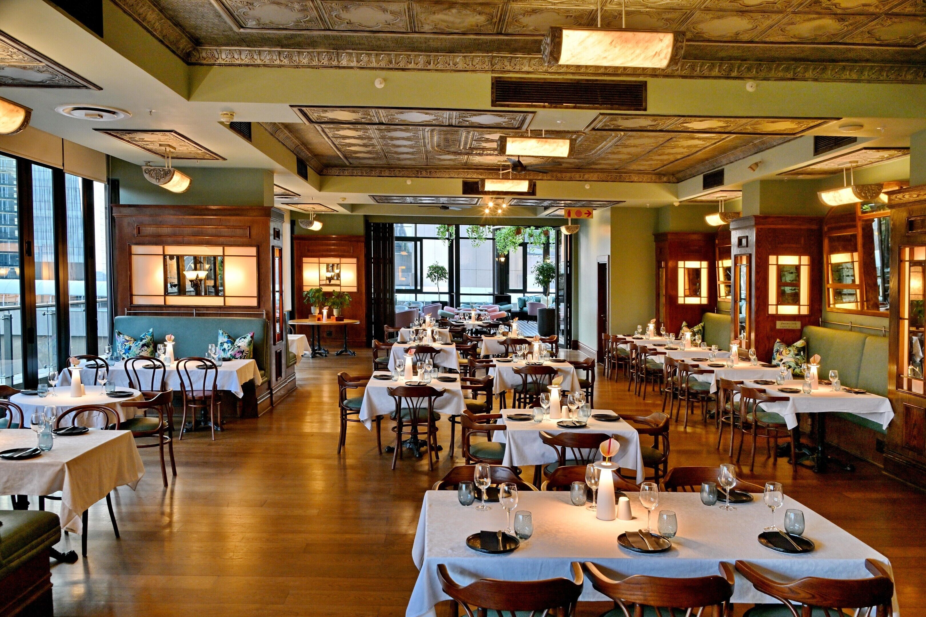 Un restaurante espacioso con varias mesas, sillas y un alto techo con detalles ornamentales.