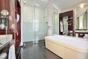 A modern bathroom with a glass-enclosed shower, a large white bathtub, and a wooden vanity with a mirror.
