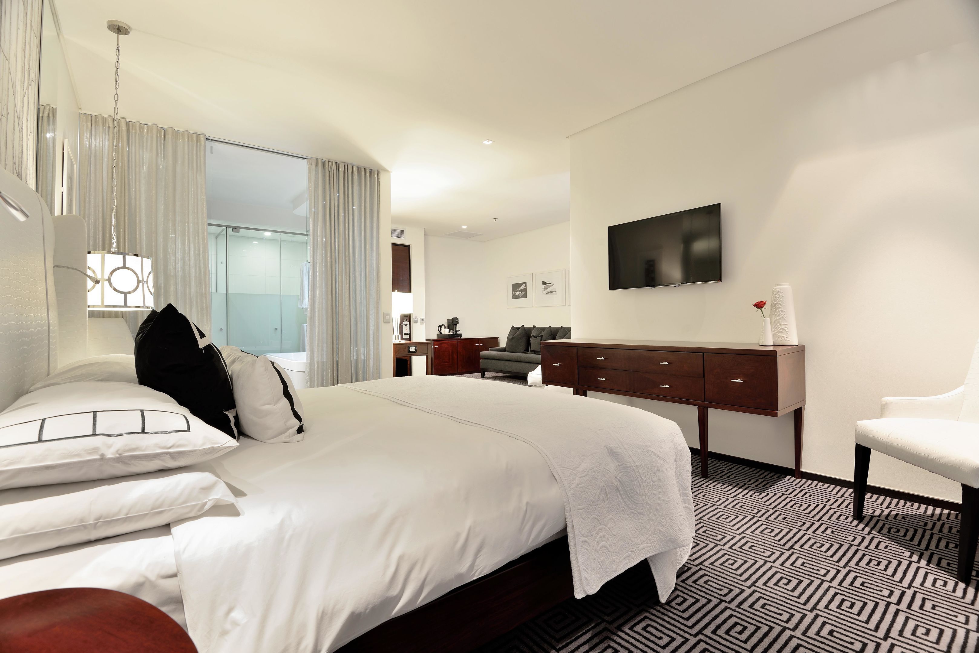 Una habitación de hotel moderna con una cama grande, un escritorio, una silla y un televisor en la pared.