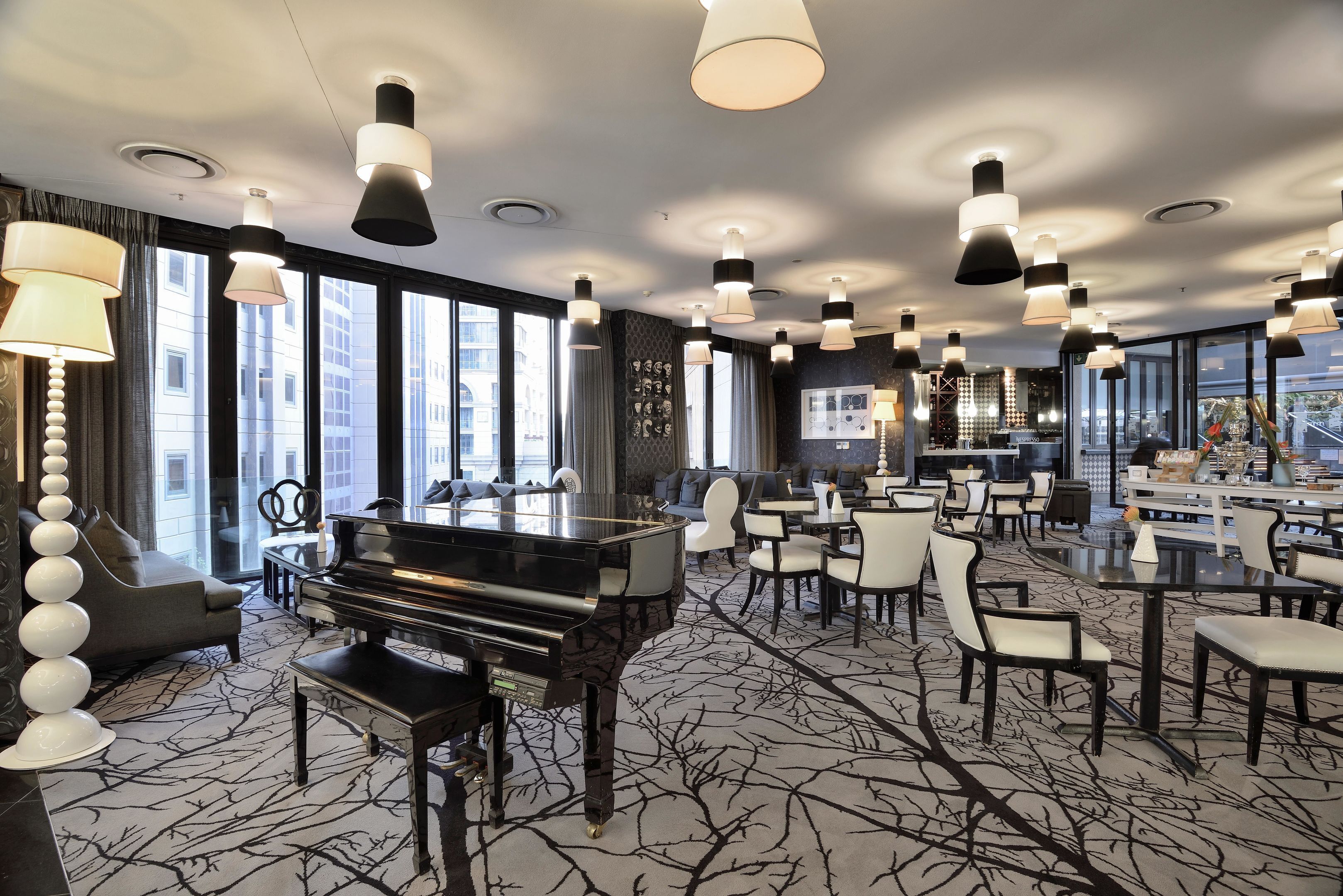Um hall de hotel espaçoso com um piano de cauda, lustres modernos e um bar.