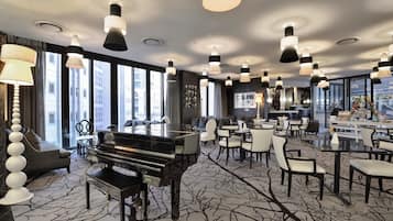 Um hall de hotel espaçoso com um piano de cauda, lustres modernos e um bar.