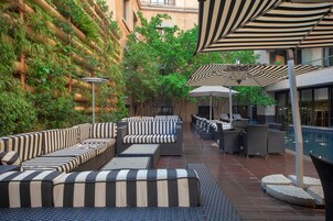 Un área de estar al aire libre con sofás a rayas y sombrillas, rodeada de vegetación y una piscina.