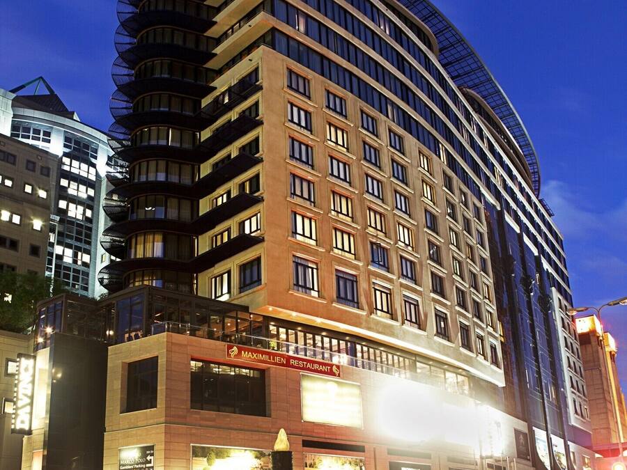 Un hotel de varios pisos con fachada curva, grandes ventanales y un restaurante en la planta baja.