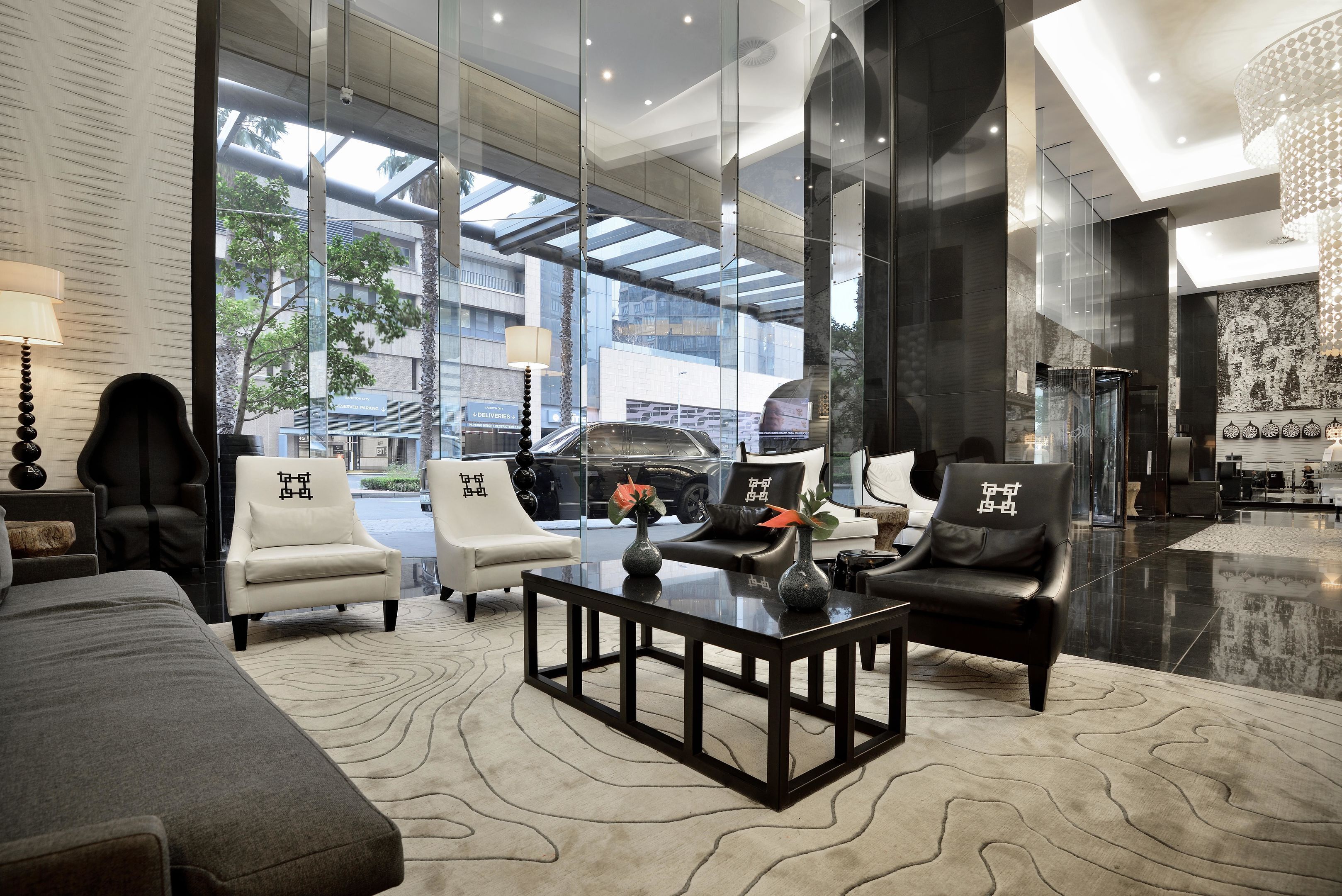 A modern lobby with a glass wall, leather chairs, a coffee table, and a patterned rug.