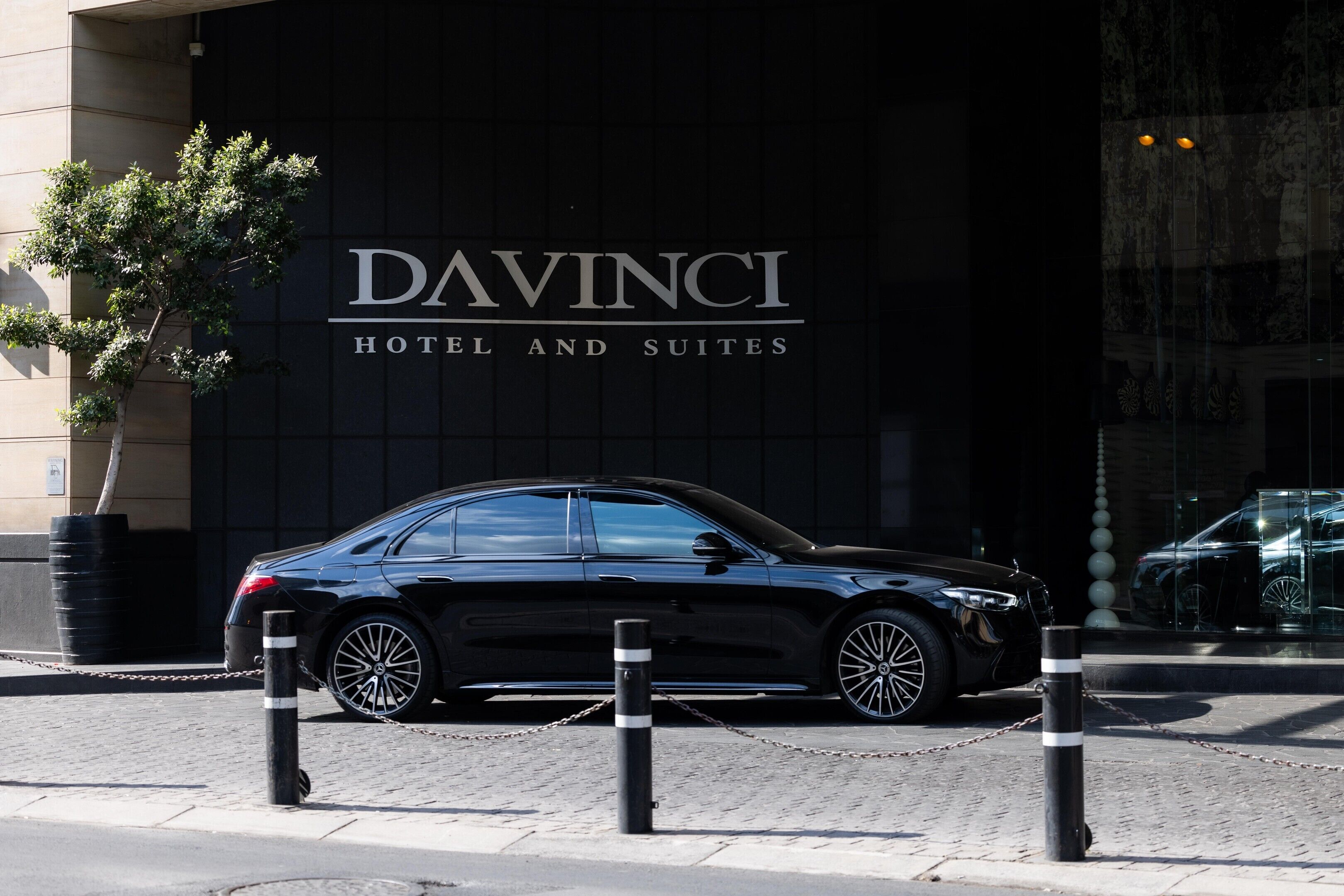 Een zwarte auto geparkeerd voor een gebouw met een bord waarop 'DAVINCI HOTEL AND SUITES' staat.