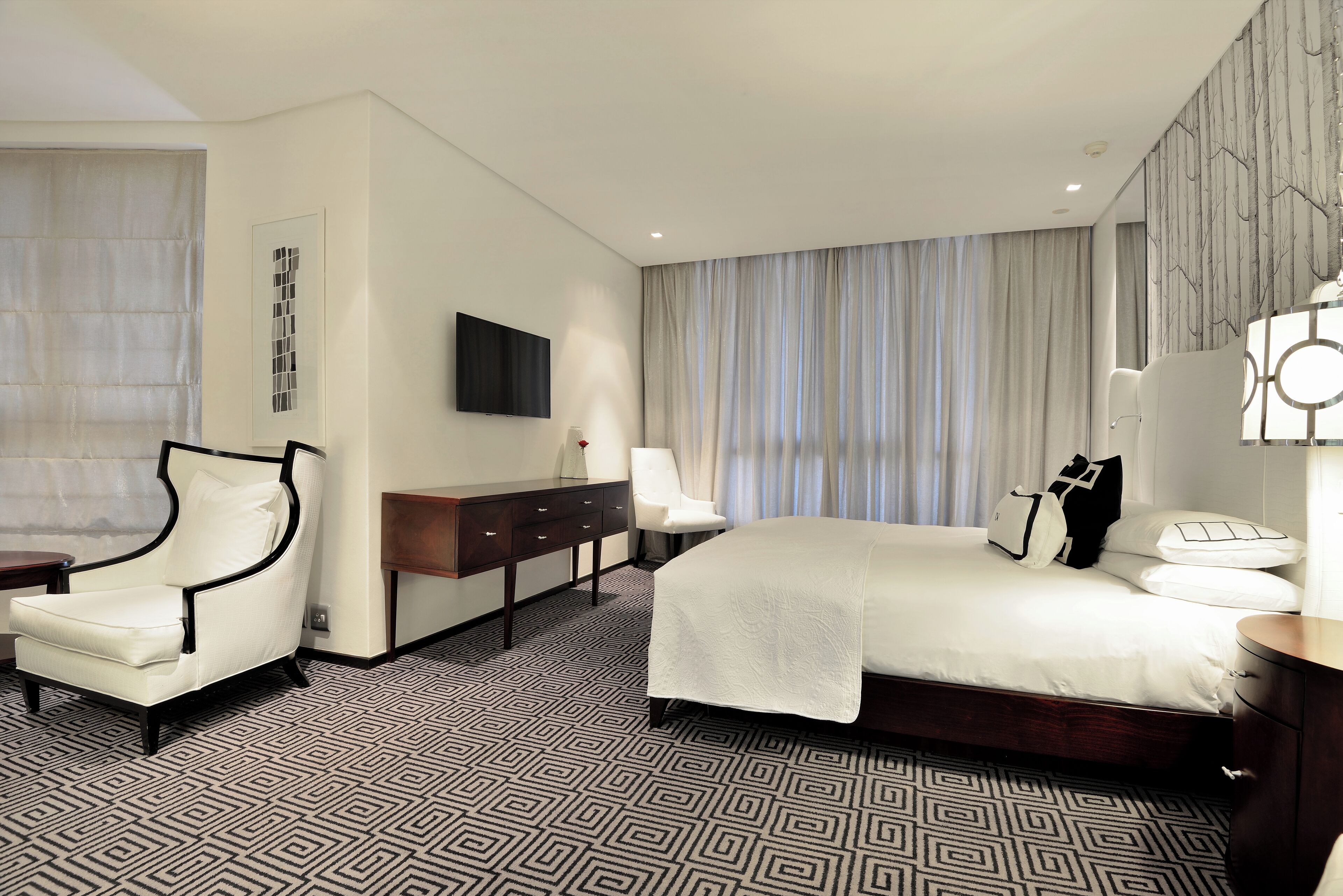 A hotel room with a large bed, a chair, a desk, and a TV on the wall.