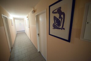 A hotel hallway with a tiled floor, framed artwork on the wall, and doors leading to rooms. - Alper Hotel am Potsdamer Platz (Berlin)