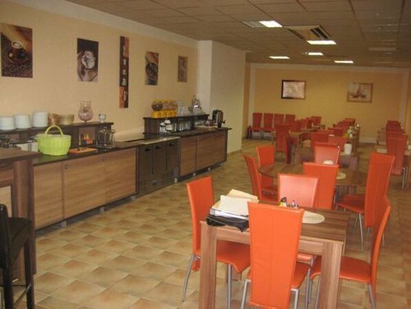 Un comedor con armarios de madera, sillas color naranja y suelo de baldosas.