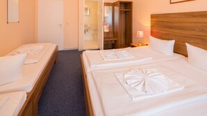 A hotel room with two beds, a wooden headboard, a mirror, a door leading to a bathroom, and a nightstand with a lamp. - Alper Hotel Am Potsdamer Platz (Berlin)