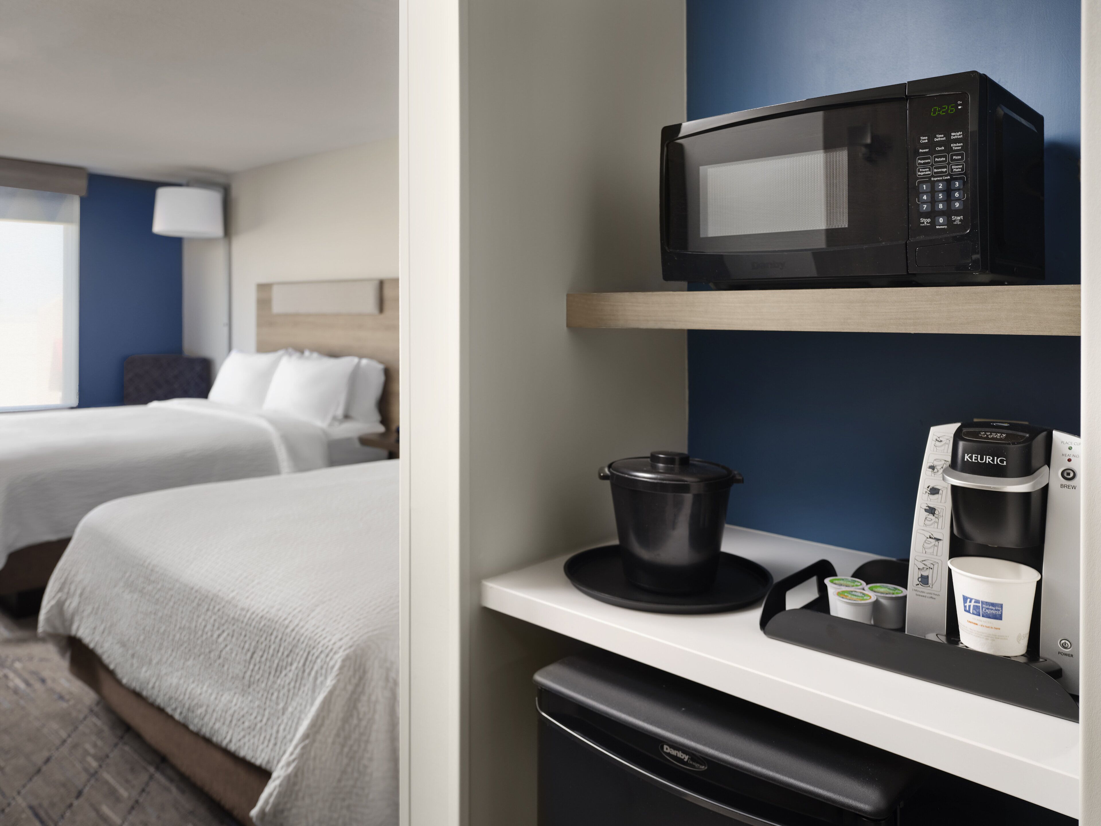 A hotel room with two beds, a microwave, a coffee maker, and a kettle on the counter.