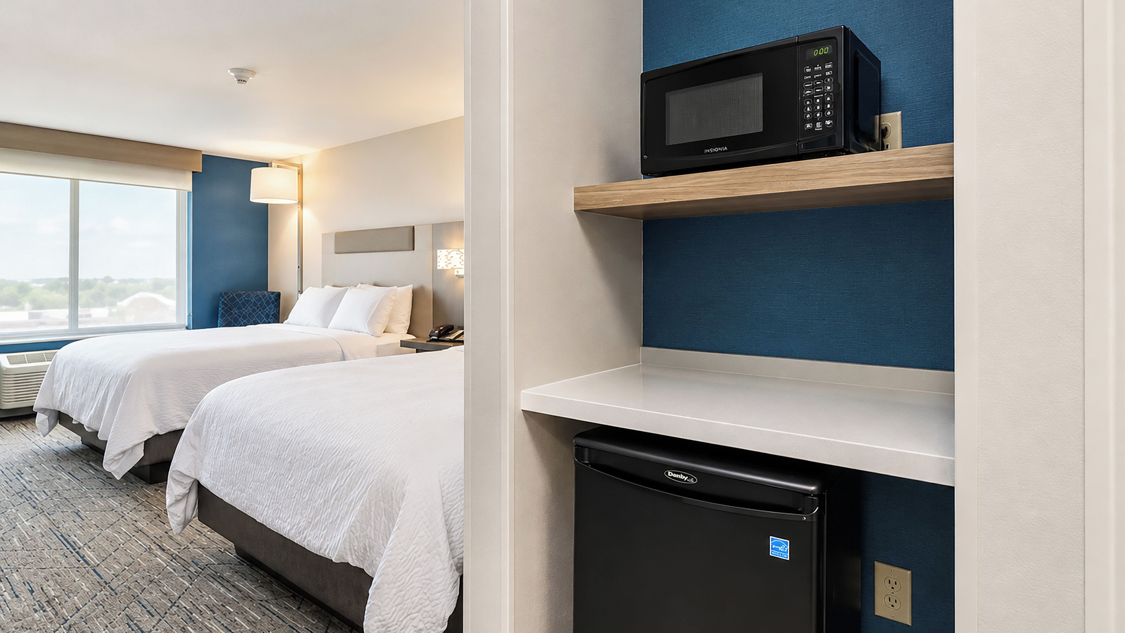 Habitación de hotel con dos camas, microondas, refrigerador y ventana con vista.