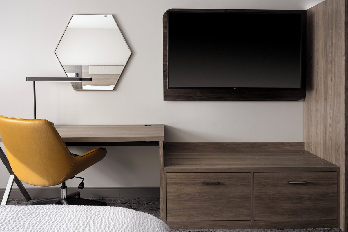 A modern room with a desk, a yellow chair, a TV mounted on the wall, and a wooden cabinet.