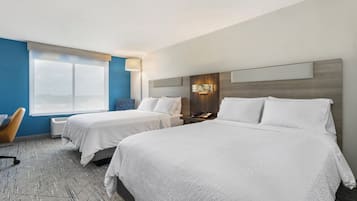 Quarto de hotel com duas camas, uma escrivaninha, uma cadeira e uma janela grande.