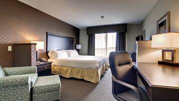 A hotel room with a bed, a desk, a chair, a nightstand, a lamp, and a window with curtains.