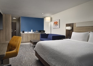 A hotel room with a bed, a desk, a chair, a sofa, a kitchenette, and a bathroom.