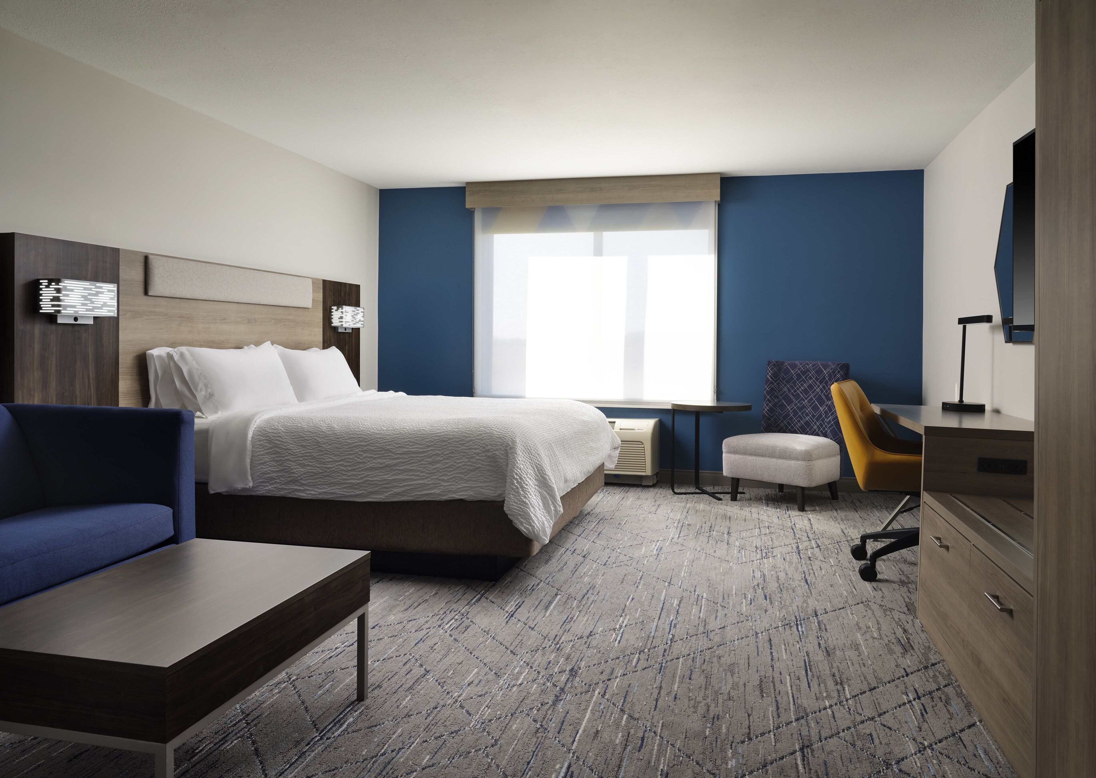Una habitación de hotel con cama, escritorio, sillón, sofá y cómoda.