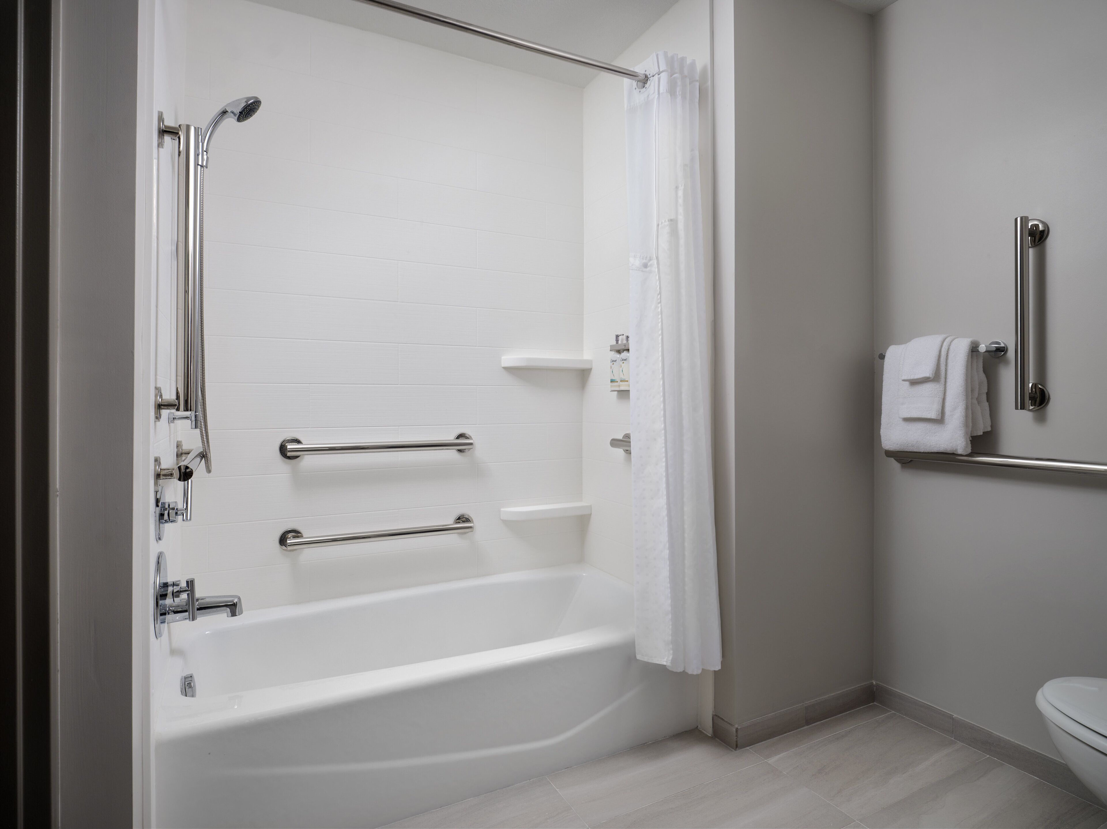 Une salle de bain moderne avec une baignoire blanche, des barres d’appui, une pomme de douche et des toilettes.