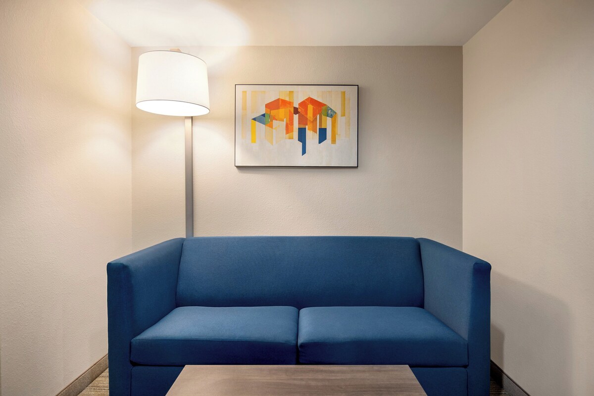 Een blauwe bank in een kamer met een enkel abstract schilderij in een lijst aan de muur en een vloerlamp.