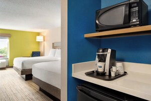 Habitación de hotel con cama, microondas, cafetera y cesto de basura.