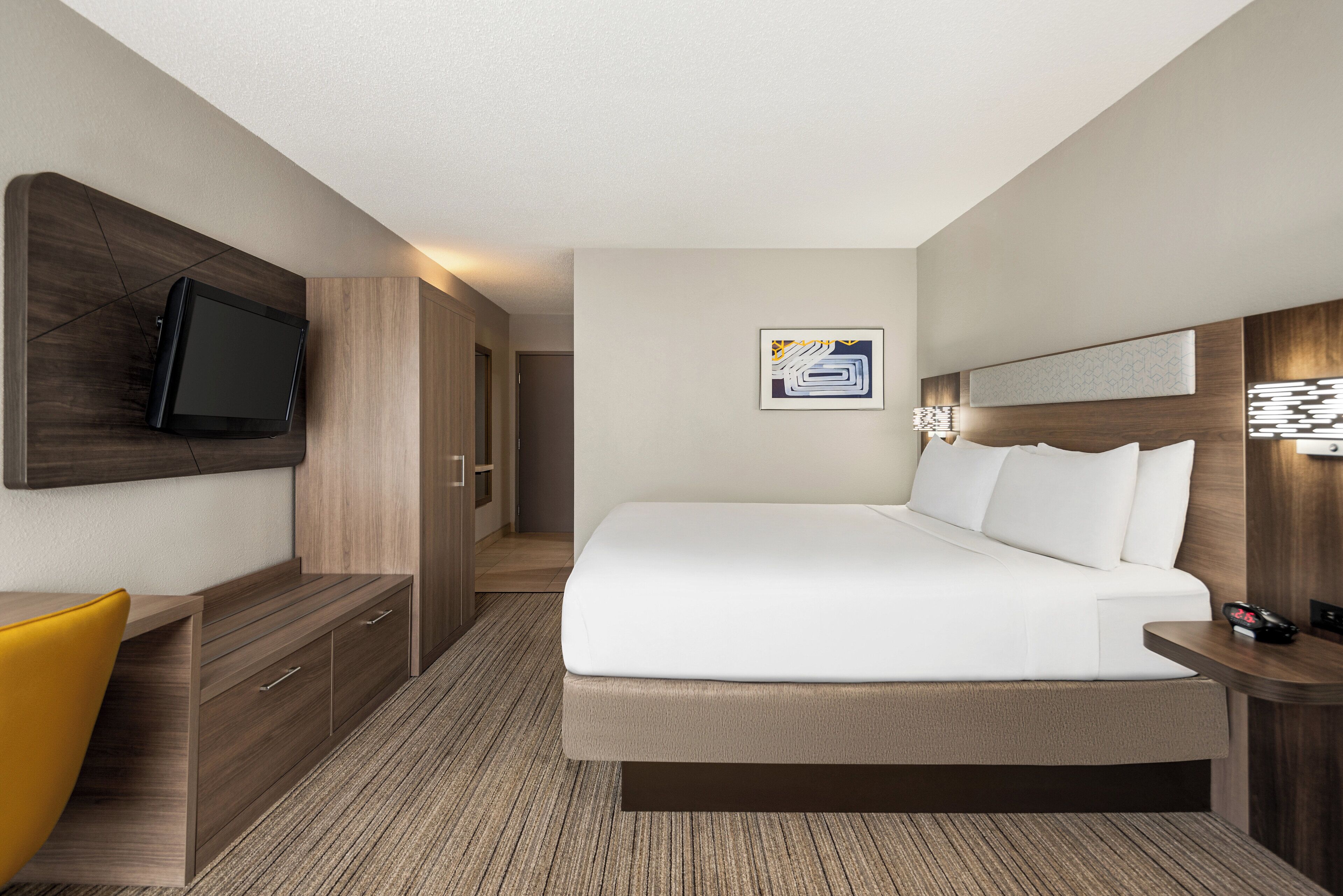 A hotel room with a bed, a desk, a television, and a door leading to a hallway.