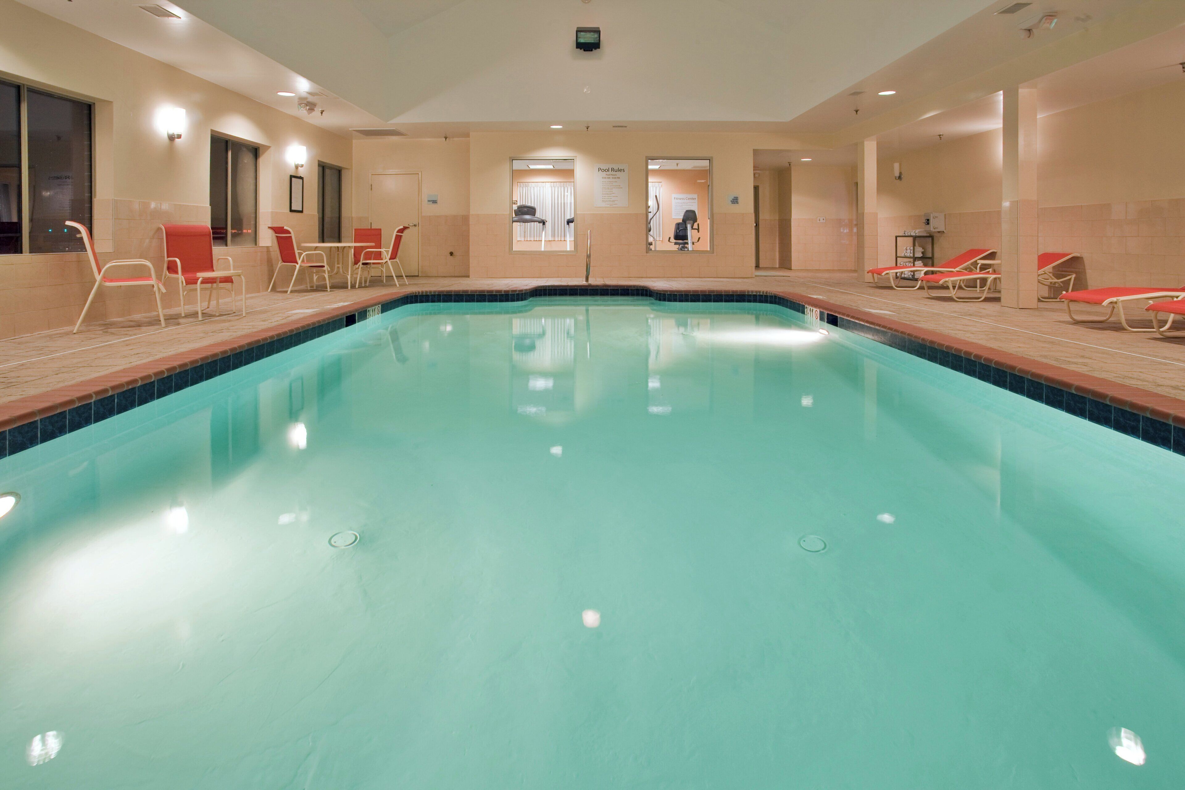 A large indoor swimming pool with lounge chairs and tables around the perimeter.