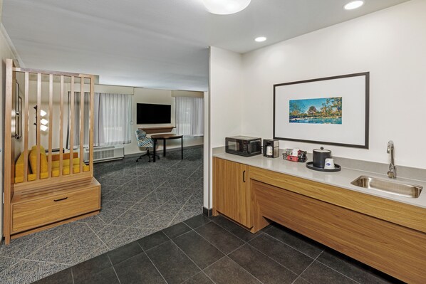 Una habitación de hotel moderna con kitchenette, zona de comedor y televisión.