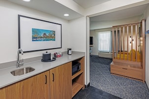 Una habitación de hotel moderna con kitchenette, un cuadro enmarcado en la pared, un mueble de madera y vistas al área de estar.